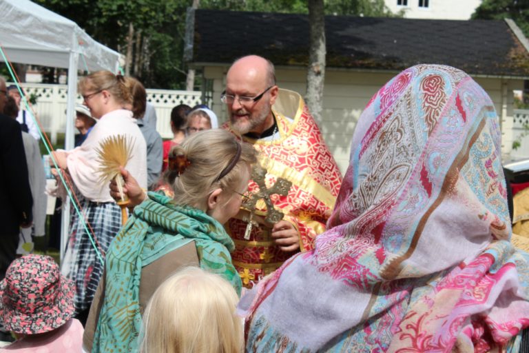 Ihmisiä ja pappi vihmoo vettä huiskalla