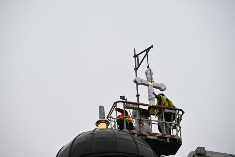 Rakennustyöntekijät nostavat ristiä paikoilleen kirkon kupolin päälle nostokorin avulla.