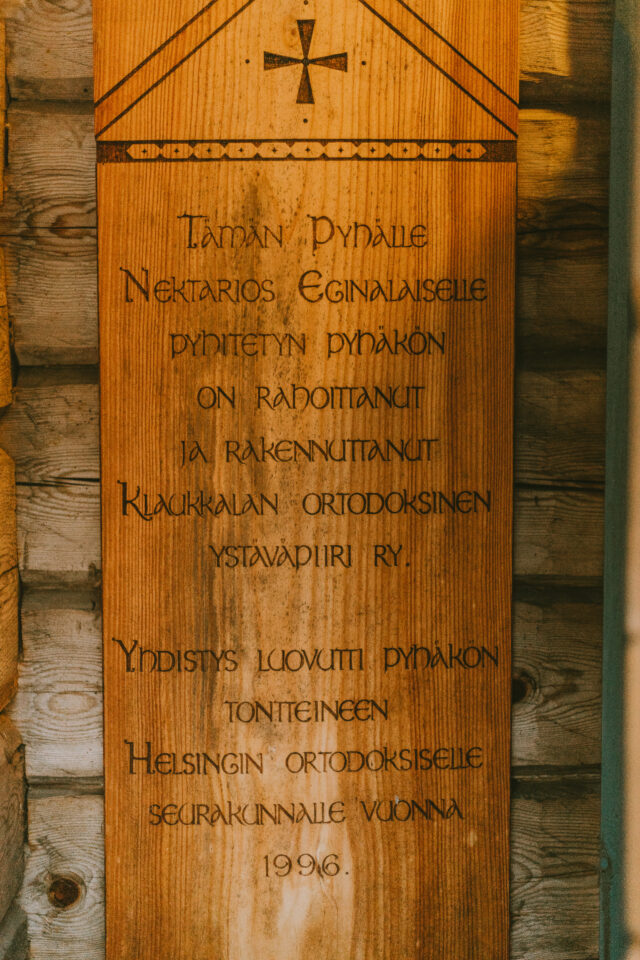 Puinen laatta, jossa ylhäällä risti ja alla teksti, jossa kerrotaan Pyhän Nektarios Eginalaiselle pyhitetyn pyhäkön rakentamisesta ja sen luovuttamisesta seurakunnalle vuonna 1996.