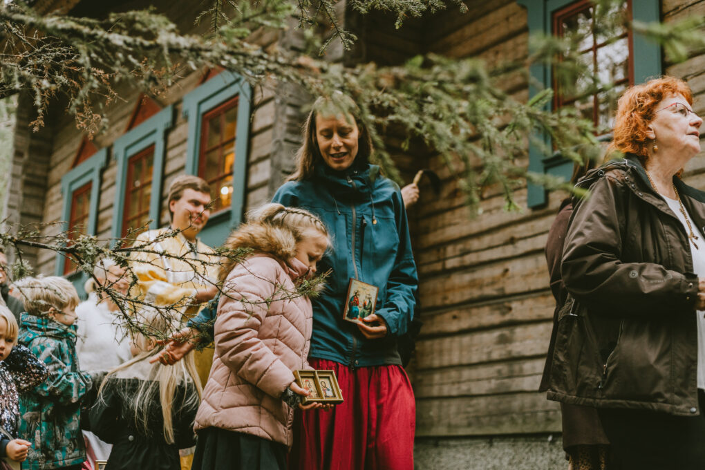 Tyttö ja äiti kävelevät kirkon ympäri. Tyttö väistää puuoksaa ja kantaa ikonia.