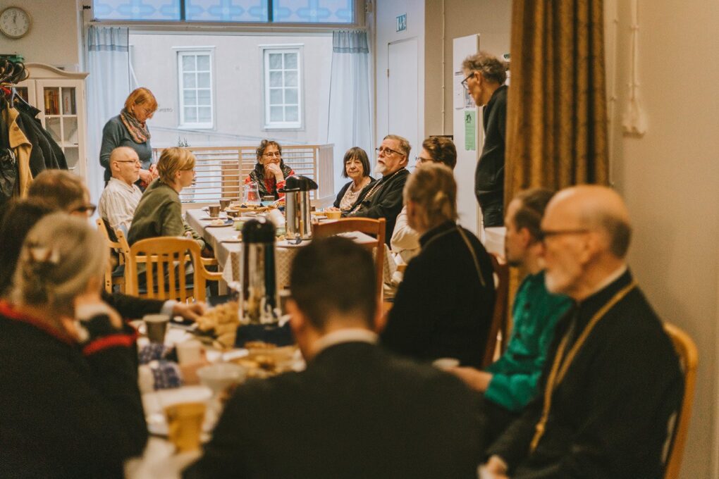 Kirkkokahvit kirkkosalissa. Ihmisiä kokoontunut ja istuu pöytien ääressä.