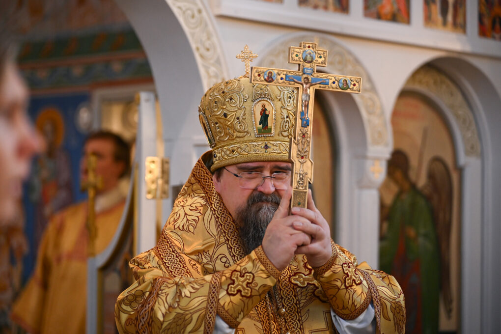 Piispa kultaisessa vaatteessa kohottaa ylös kultaisen ristin kirkossa. 