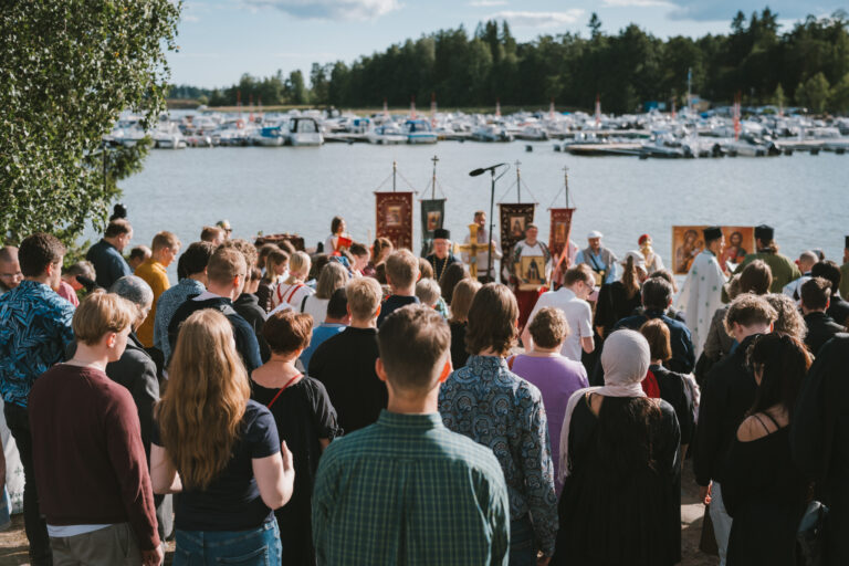 Ihmisiä kokoontuneena Otsolahden rantaan Espoon Tapiolassa. Etualalla näkyvät kirkkoliput ja risti sekä lyhty.
