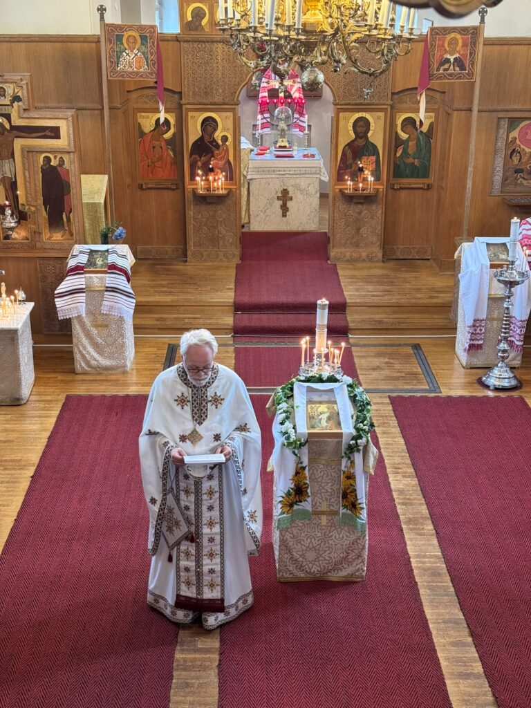 Isä Heikki Huttunen seisoo profeetta Elian kirkon ikonostaasin edessä ja pitää käsissään tekstiä.
